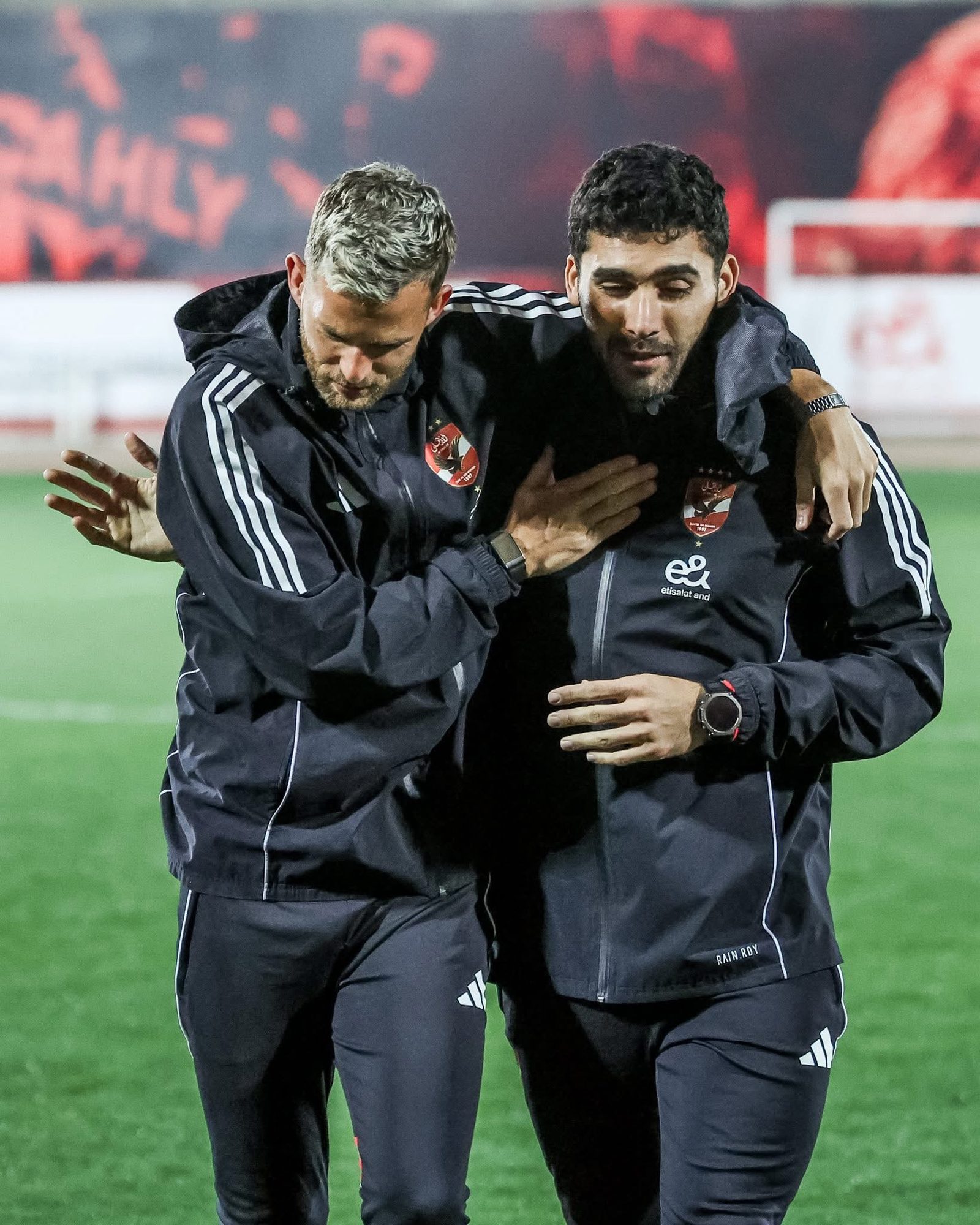 Shihy and a colleague arm in arm on the pitch